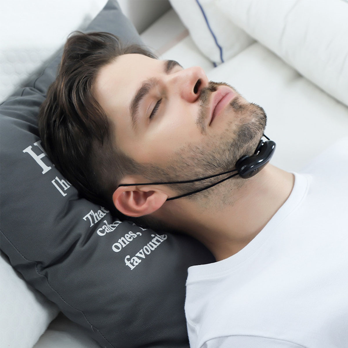 Mann mit Nackenmassagegerät auf grauem Kissen, liegend. Der Mann hat die Augen geschlossen.