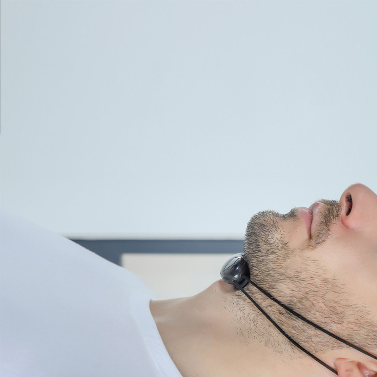 Ein Mann, der ein schwarzes Nackenmassagegerät trägt, liegt, weißer Hintergrund.