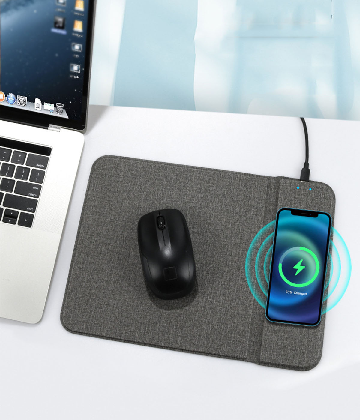 Eine schwarze Maus und ein Telefon, das auf einem grauen Mauspad geladen wird. Laptop im Hintergrund.