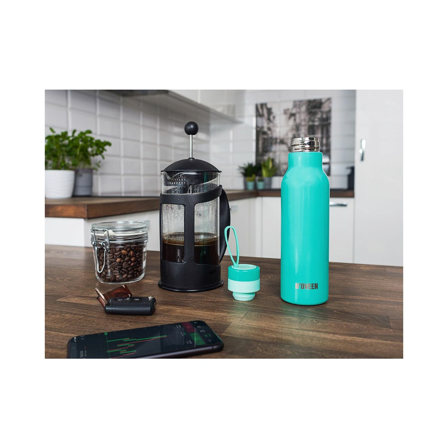 French Press, Wasserflasche, Kaffeebohnen und Smartphone auf einem Holztisch.