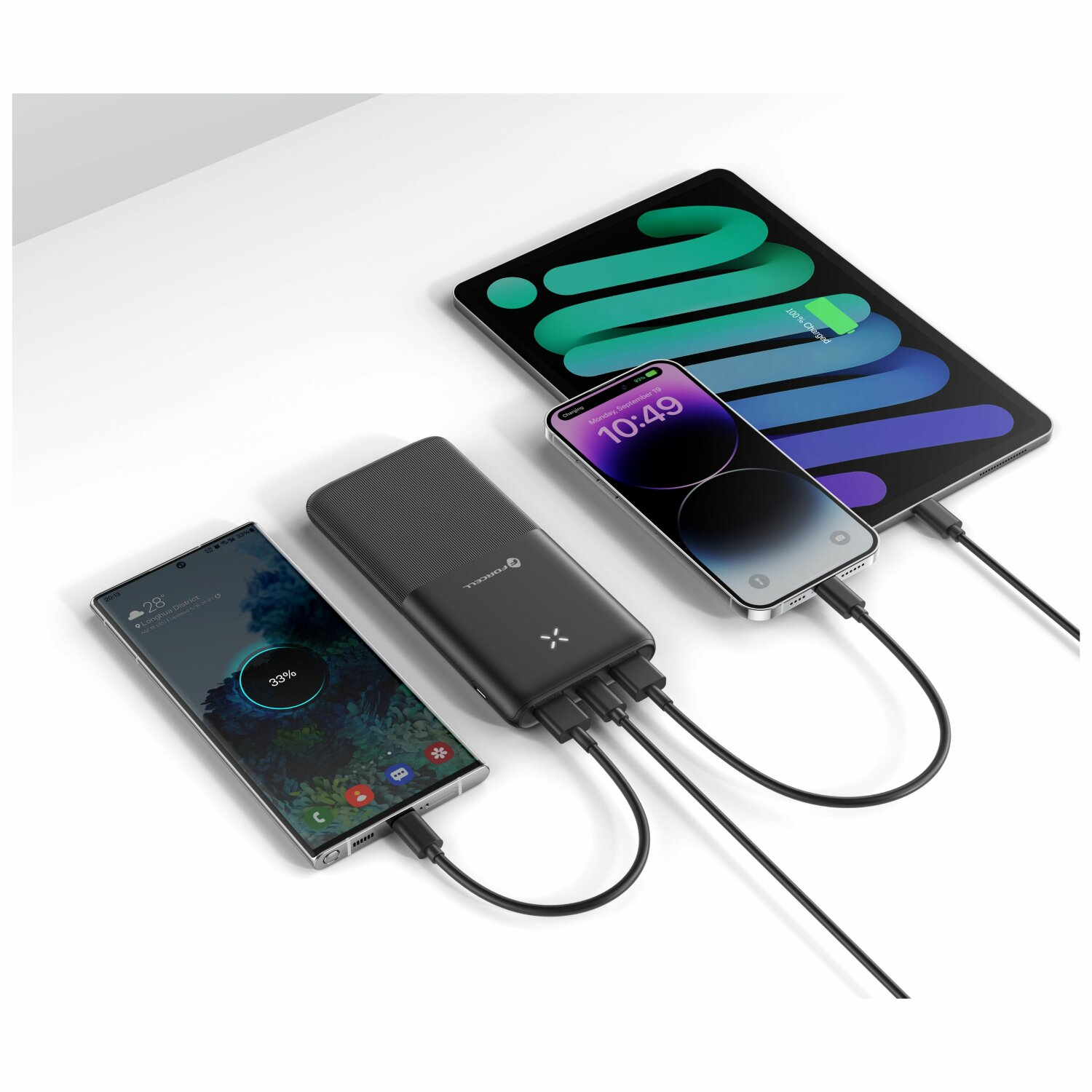 Telefone und ein Tablet, die von einer Powerbank auf einer weißen Oberfläche geladen werden.