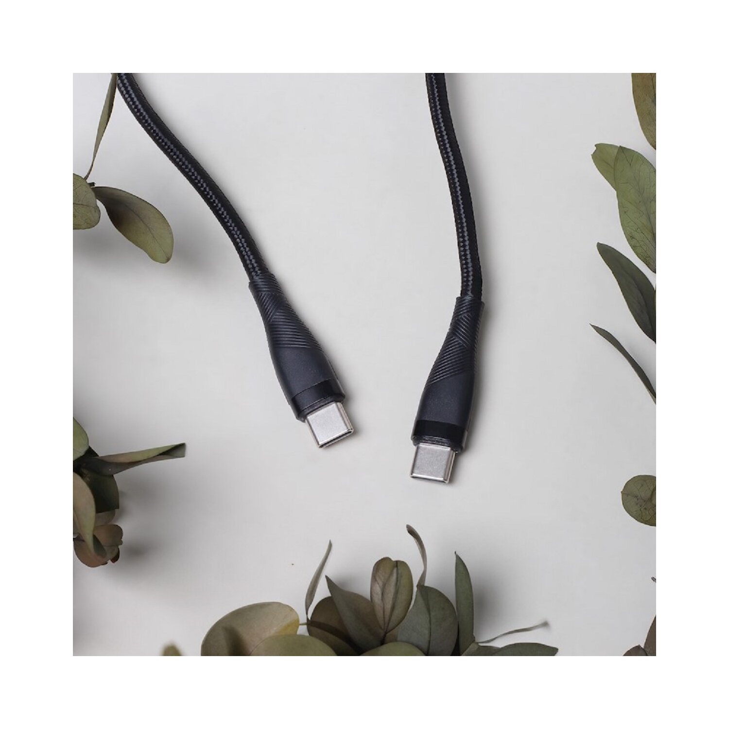 Schwarze USB-C-Kabel mit Steckern. Blätter auf hellem Hintergrund. Draufsicht.