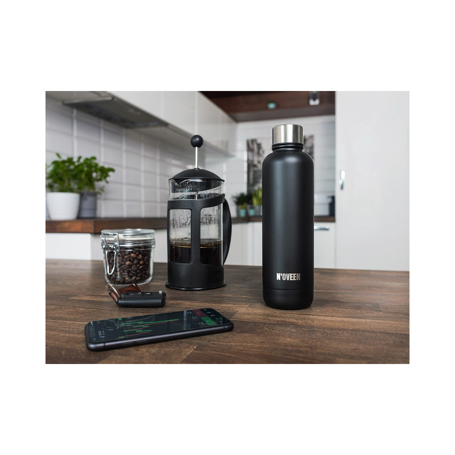 Eine schwarze Wasserflasche und ein Kaffee-Setup auf einem Holztisch: Bohnen, French Press und ein Telefon.