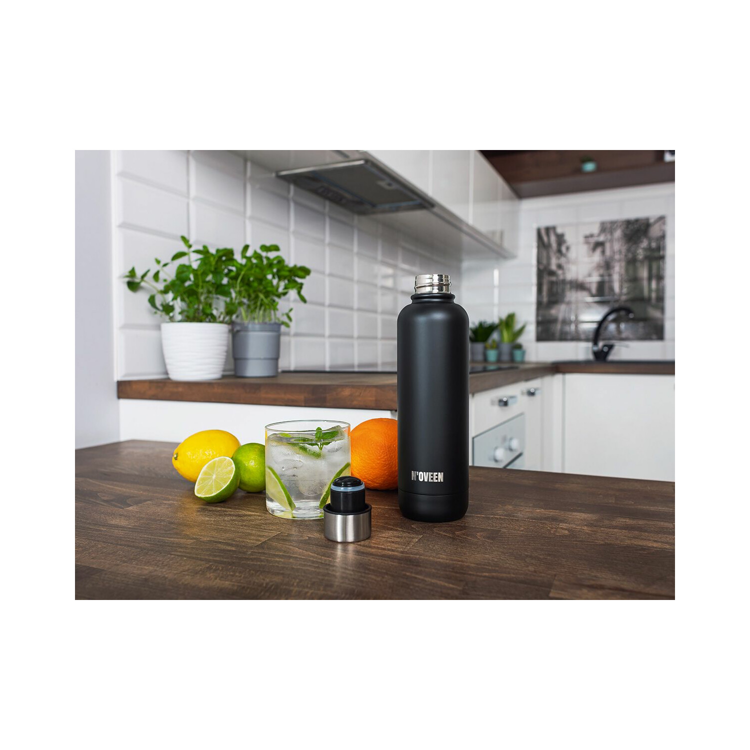 Eine schwarze Wasserflasche mit silbernem Deckel und ein Glas Wasser mit Früchten daneben.