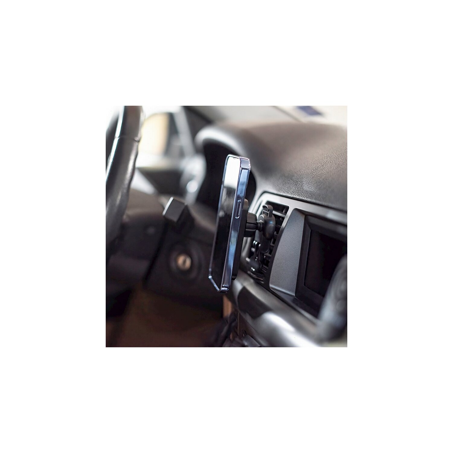 Schwarzes Telefon in der Lüftung eines Autos montiert, Armaturenbrett sichtbar.