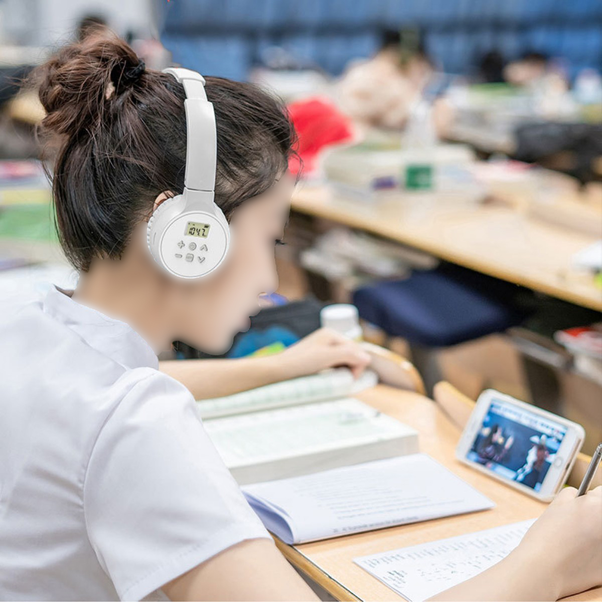 Eine Frau mit Kopfhörern, die auf ein Telefon schaut, sitzt in einem Klassenzimmer an einem Schreibtisch.