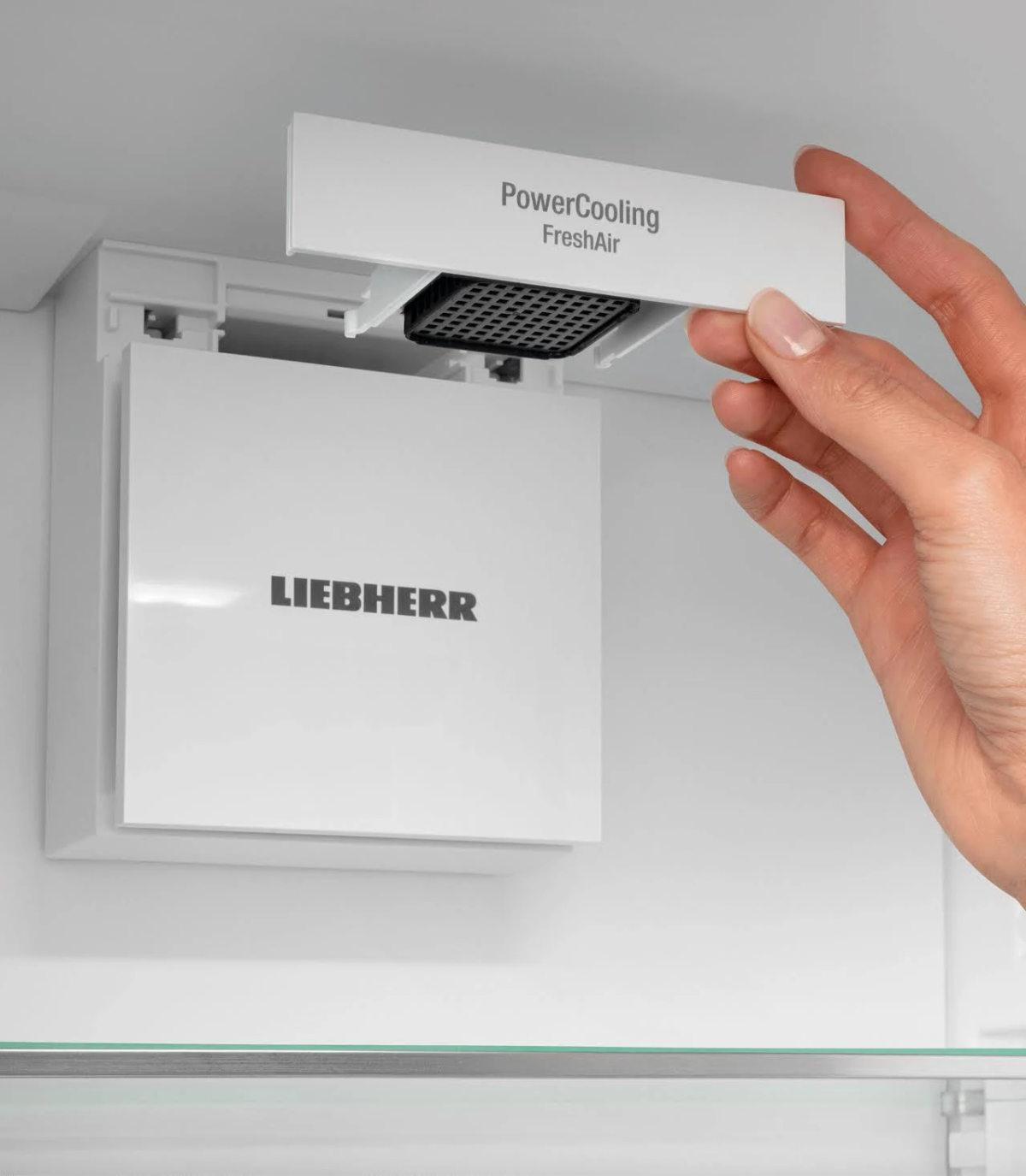Una mano abriendo un componente blanco de refrigerador con la etiqueta 'PowerCooling FreshAir'.