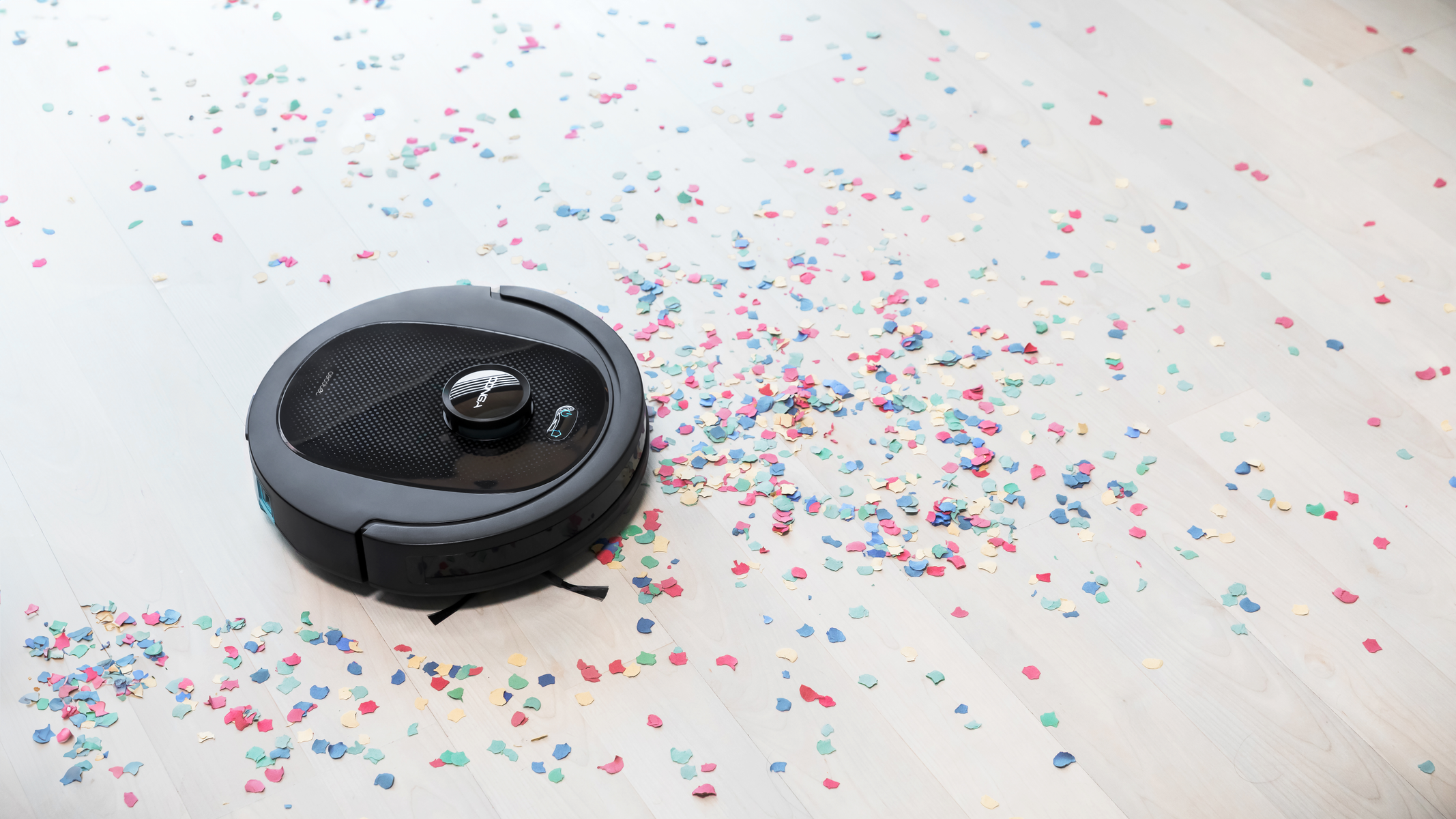 Una aspiradora robot en un piso cubierto de confeti colorido, limpiando el desorden.