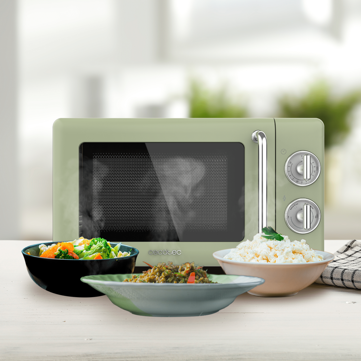 Zielona kuchenka mikrofalowa z trzema miskami jedzenia na stole i rozmytym tłem.