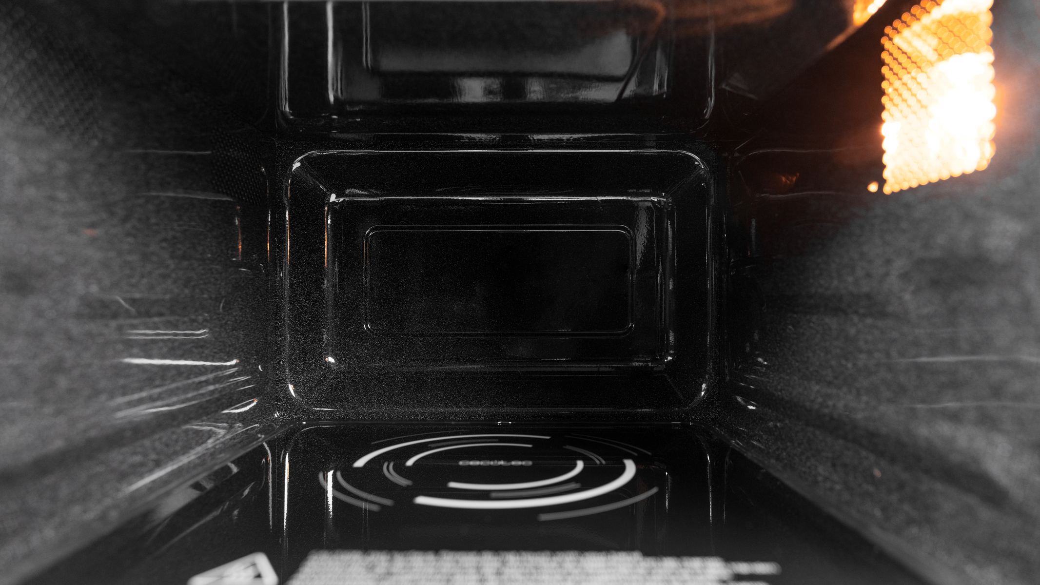 Wnętrze kuchenki mikrofalowej, pokazujące pustą, czarną wnękę i świecące źródło światła.