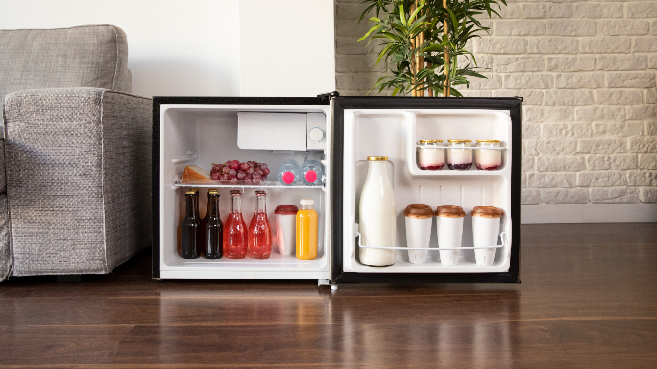 Un piccolo mini-frigo aperto pieno di bevande e snack su un pavimento di legno.