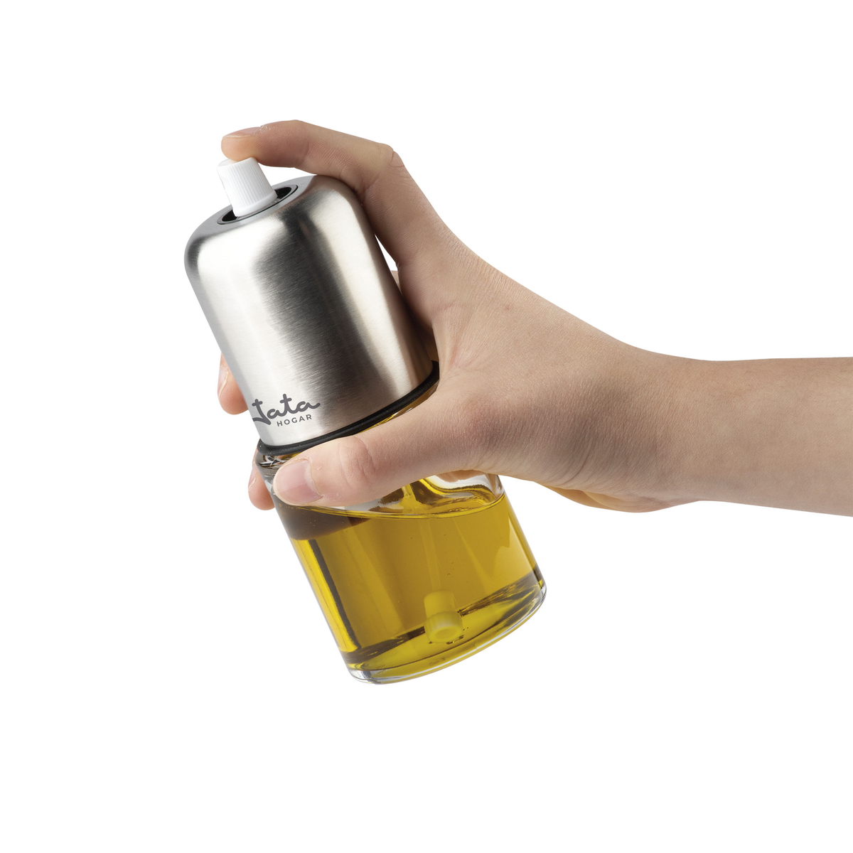Una mano sosteniendo un pulverizador de aceite de oliva. Tapa plateada, botella transparente con aceite visible.