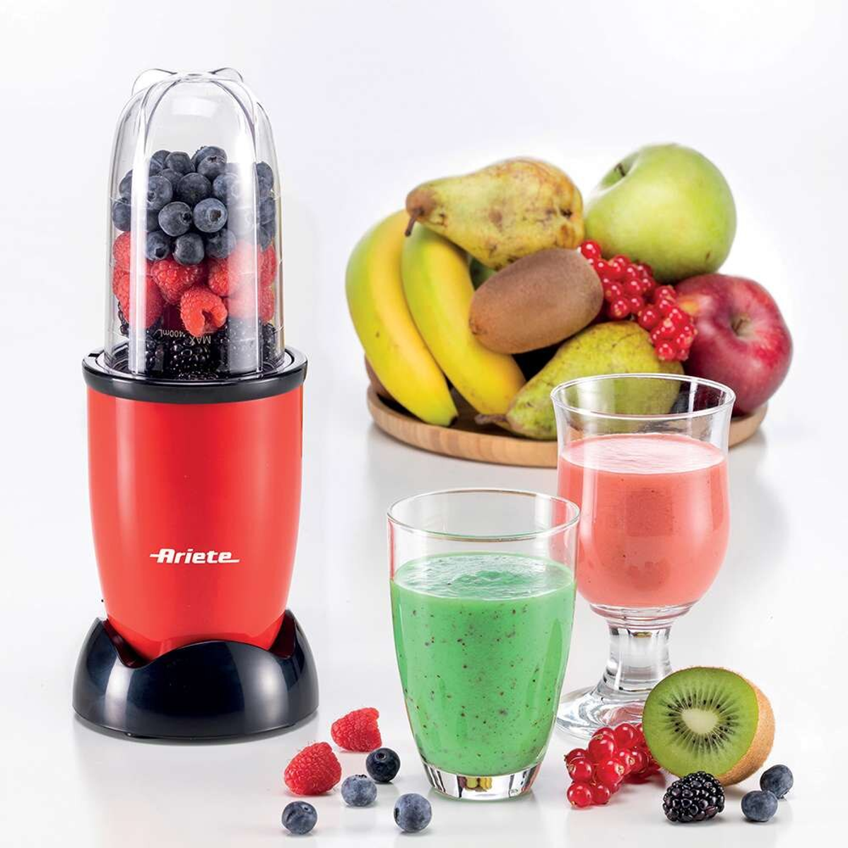 Licuadora roja con frutas y tres vasos con batidos. Frutas en el fondo.