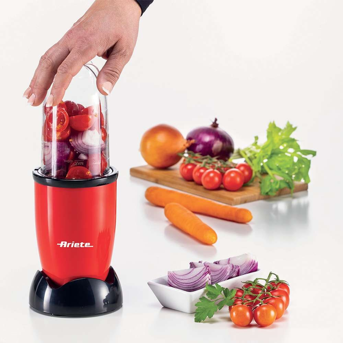 Un procesador de alimentos rojo con tomates y cebollas picadas, y otros ingredientes.