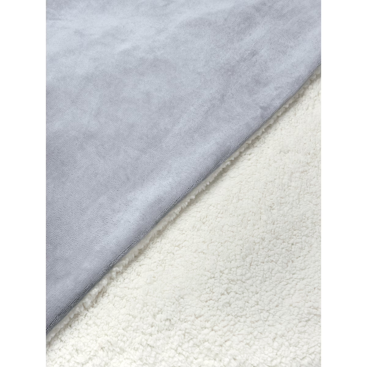 Manta gris y blanca, con textura suave y esponjosa en el lado blanco.