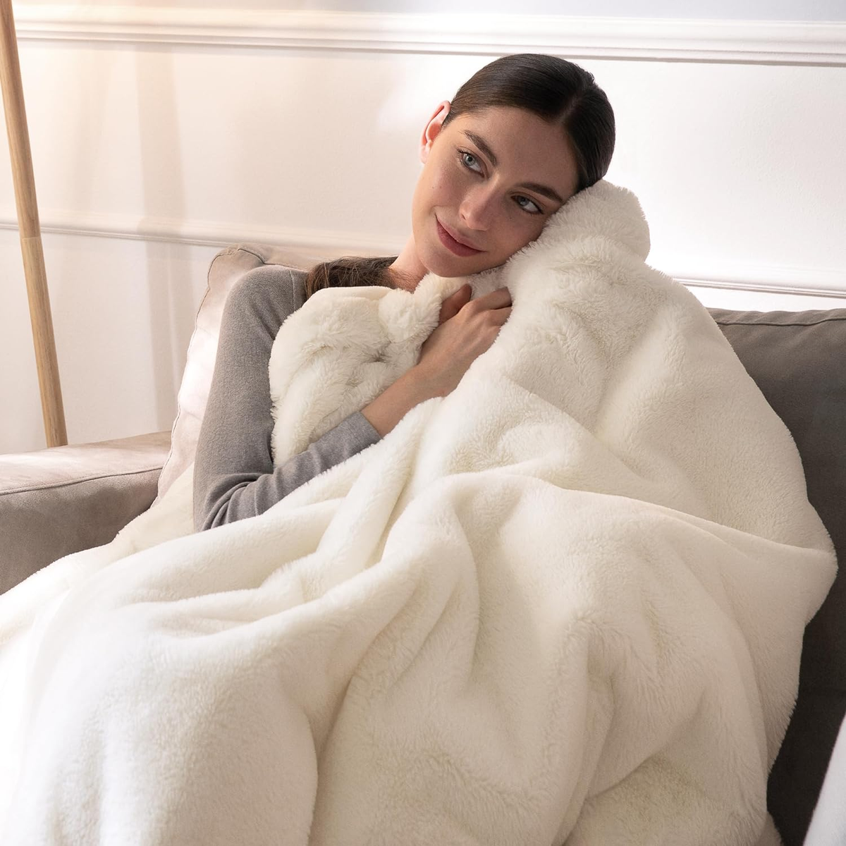 Donna sul divano, che abbraccia una coperta bianca e soffice.