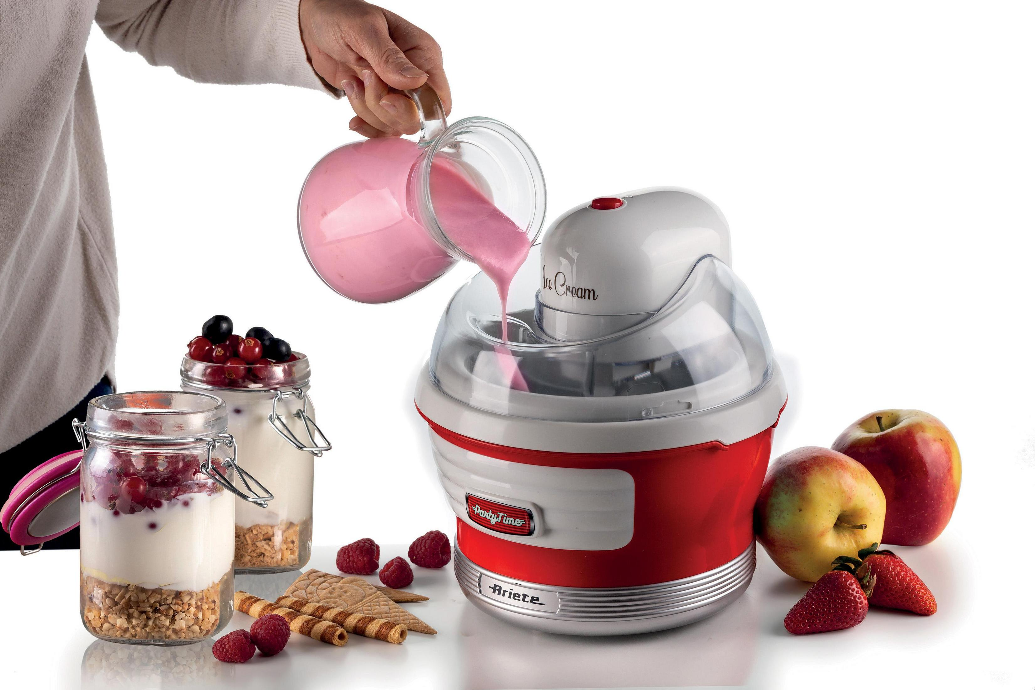 Eine Person gießt pinke Flüssigkeit in eine rot-weiße Eismaschine. Zutaten und Früchte liegen auf dem Tisch.