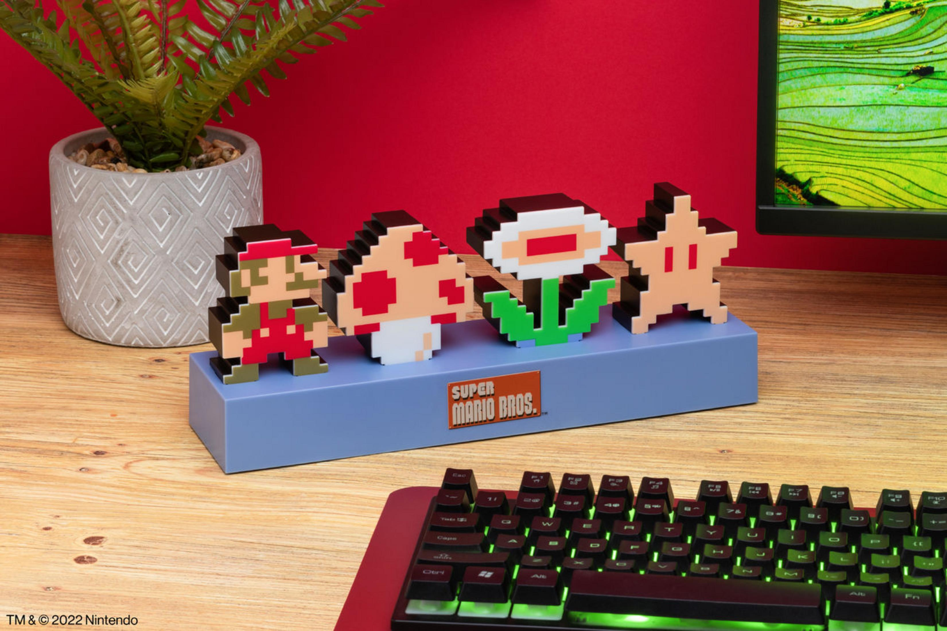 Spikselowane postacie Super Mario na niebieskim stojaku: Mario, grzyb, kwiat i gwiazda. Klawiatura na pierwszym planie.