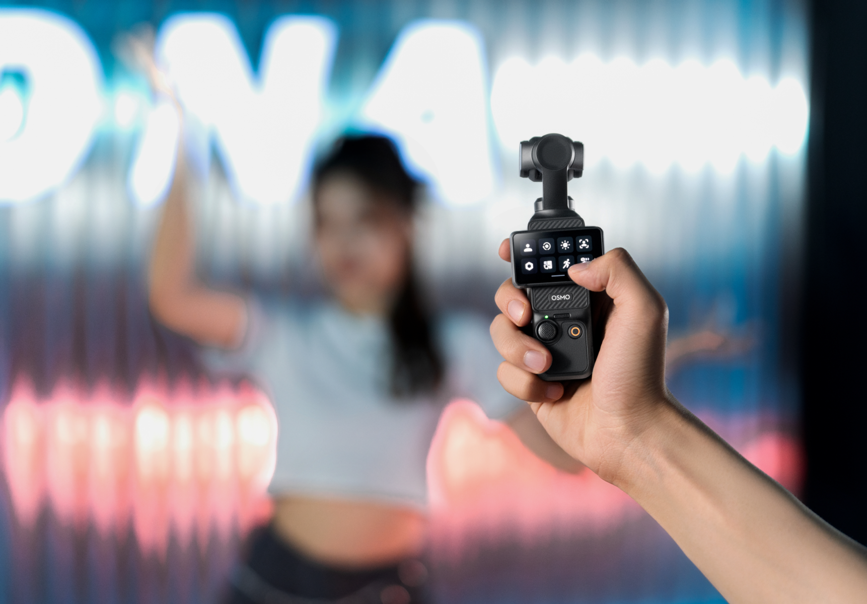 Eine Person hält einen schwarzen Gimbal-Stabilisator, mit verschwommenem Hintergrund einer Tanzenden.