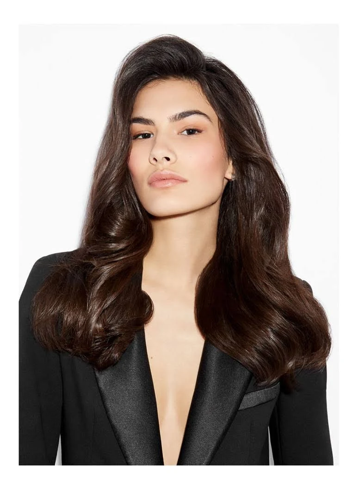 Une femme aux longs cheveux foncés et ondulés, portant un blazer noir, pose pour une photo.
