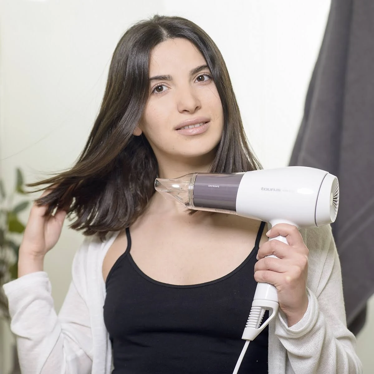 Mujer secándose el pelo con un secador de pelo blanco y morado, mirando a la cámara.