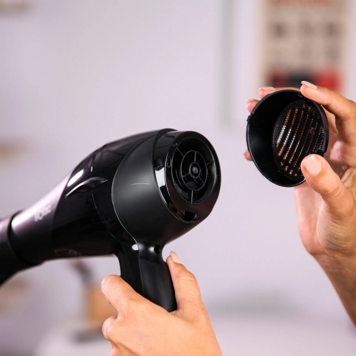 Ręce osoby trzymające czarną suszarkę do włosów i nasadkę dyszy.