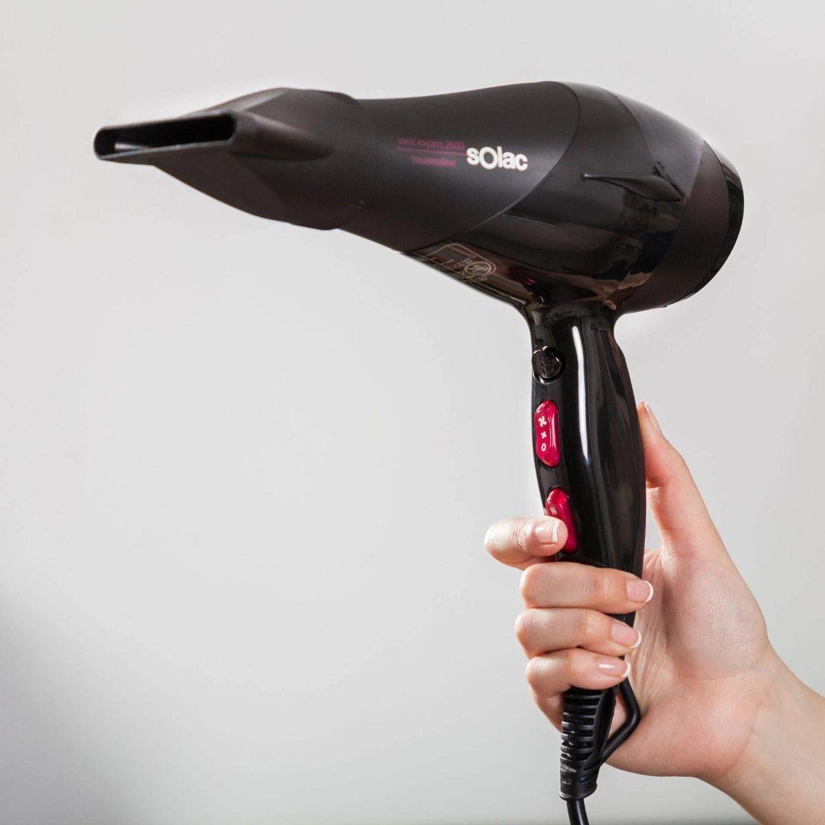 Czarna suszarka do włosów trzymana w dłoni, z czerwonymi przyciskami, na białym tle, szary uchwyt.