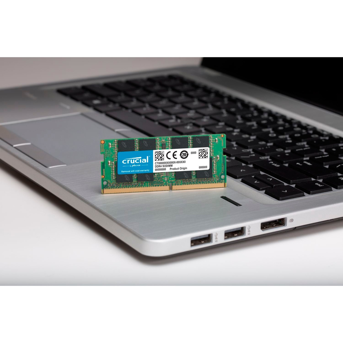 Ein Laptop mit einem Crucial RAM-Modul auf dem Touchpad. Der RAM-Riegel ist grün mit blauen und weißen Etiketten.