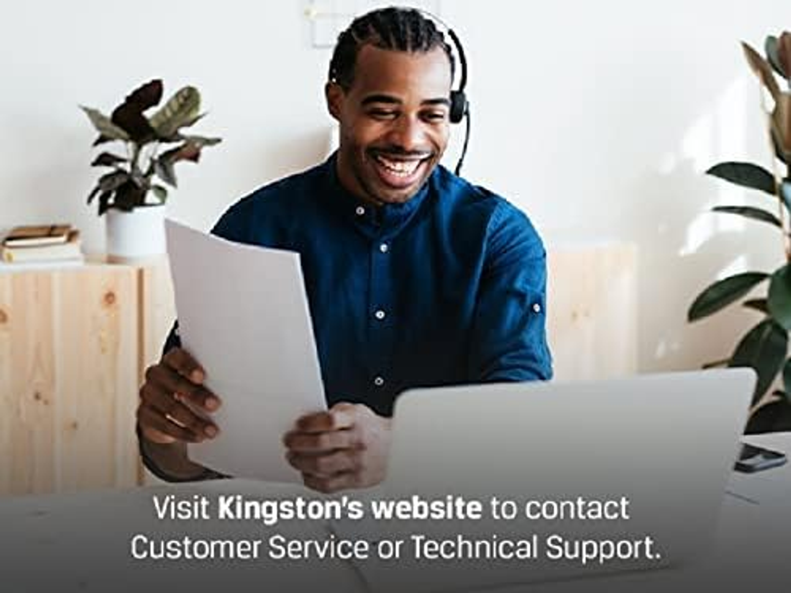 Mężczyzna z zestawem słuchawkowym uśmiecha się, trzymając papiery i patrząc na laptopa.