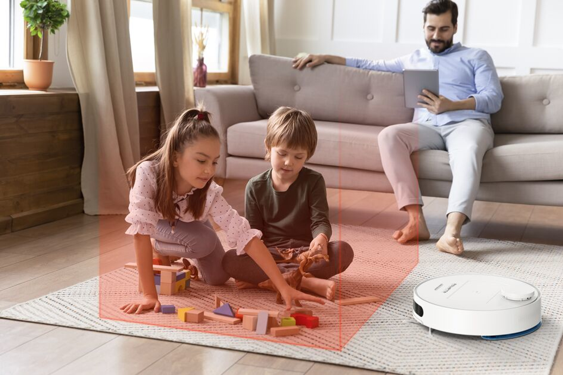 Dwójka dzieci bawiących się klockami, robot sprzątający i mężczyzna na kanapie.