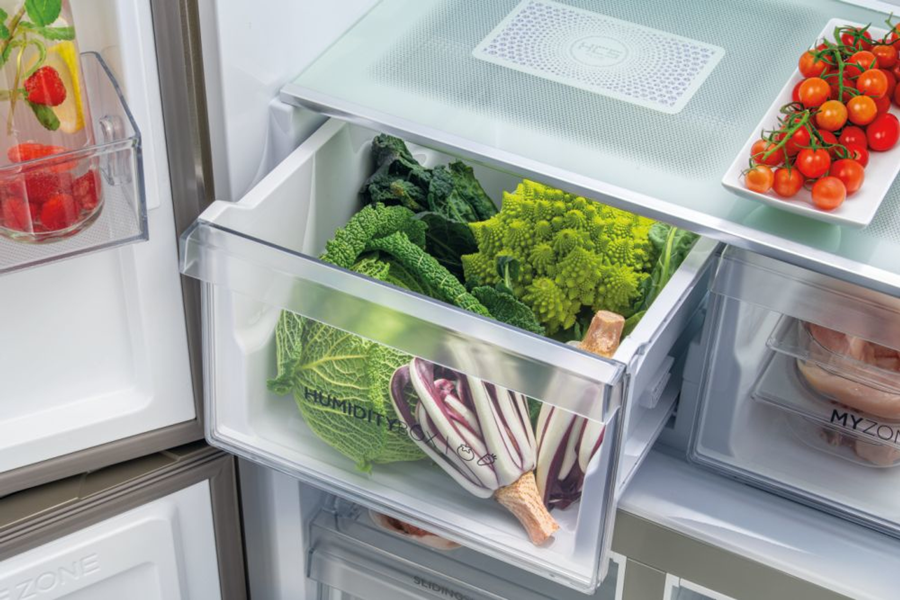 El interior de un refrigerador con cajones. Los cajones contienen verduras, tomates y otros artículos.