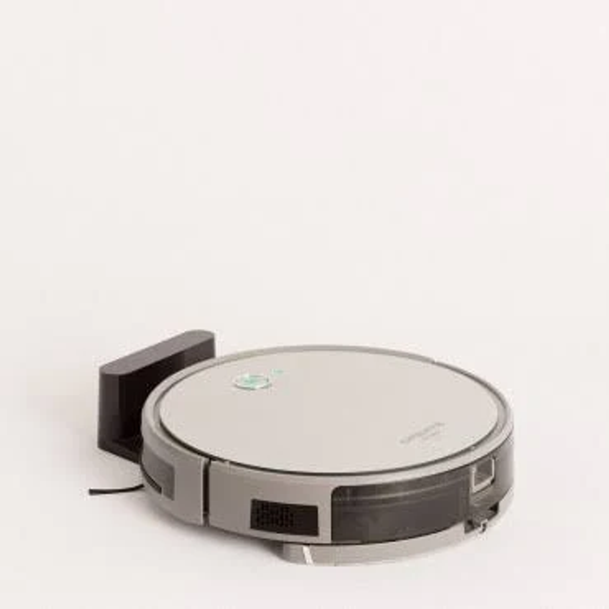 Aspiradora robot plateada con estación de carga negra sobre fondo blanco.