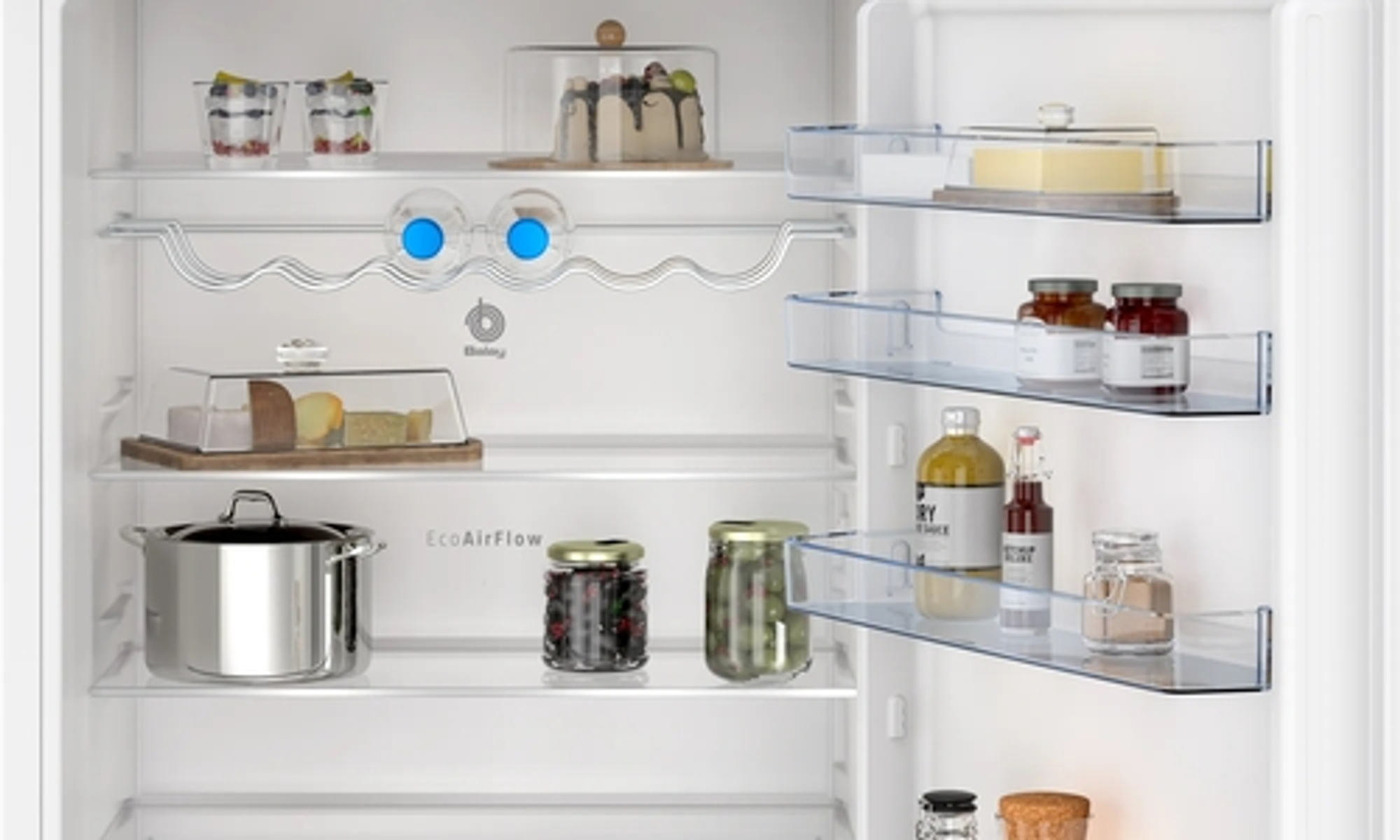 Un refrigerador abierto lleno de alimentos, incluyendo frascos, queso y pasteles. Estantes visibles.