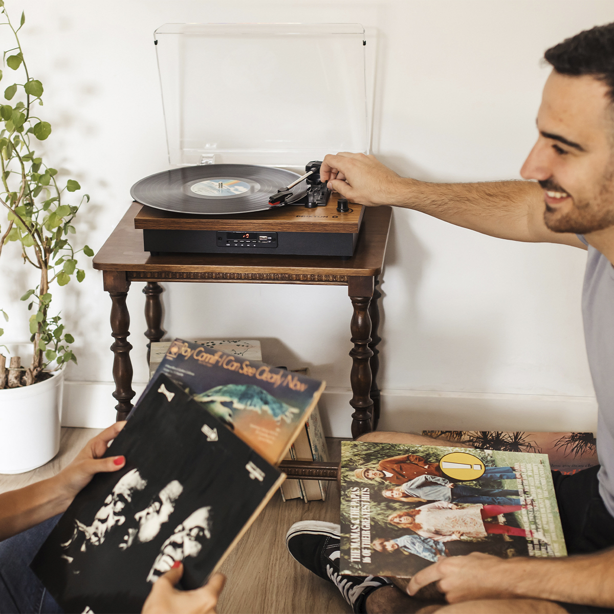 Mężczyzna w pobliżu gramofonu z płytą. Inna osoba trzyma płytę. Tło to biała ściana.