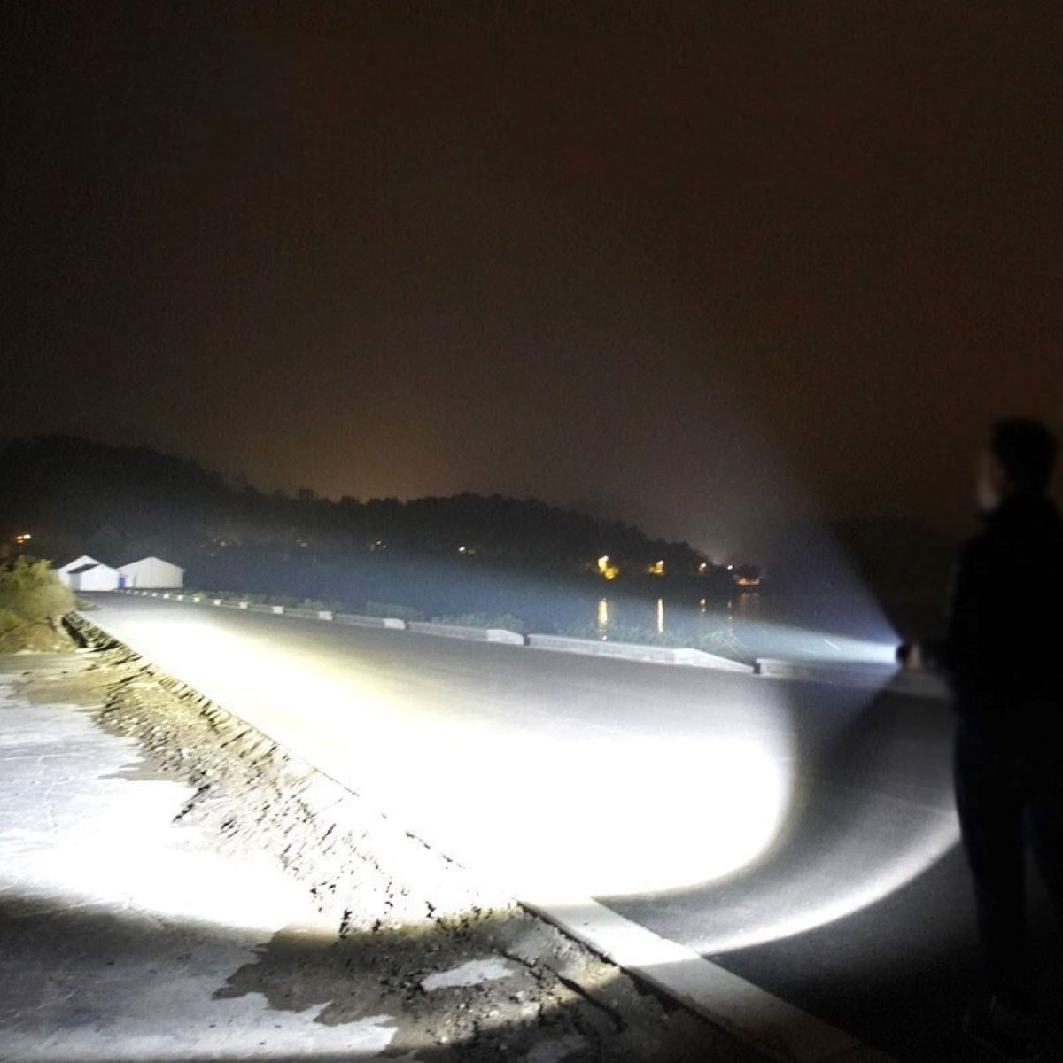 Nachtszenario: eine Person mit einer hellen Taschenlampe auf einer Straße, die die Umgebung ausleuchtet.
