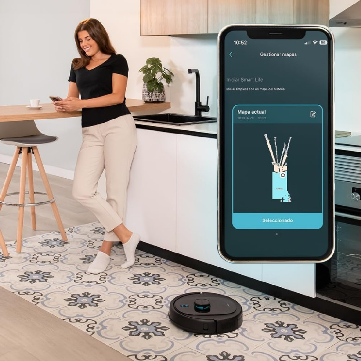 Donna che usa uno smartphone vicino a una cucina con un robot aspirapolvere. Il telefono mostra una mappa di pulizia.