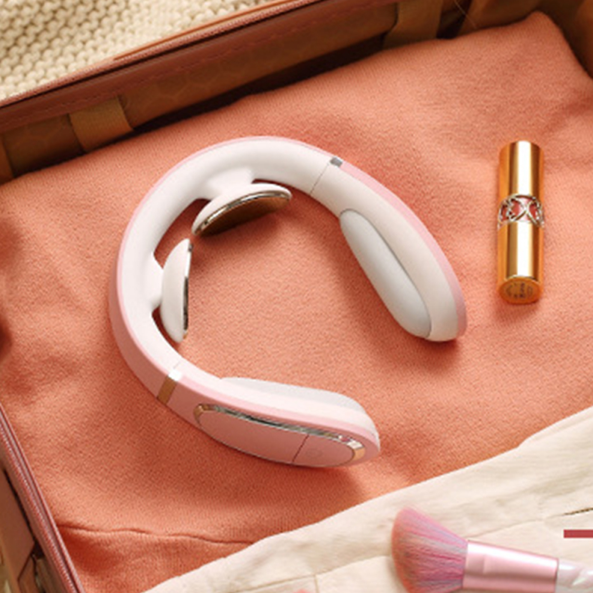 Ein Nackenmassagegerät, Lippenstift und ein Make-up-Pinsel in einem Koffer auf einem Flatlay.