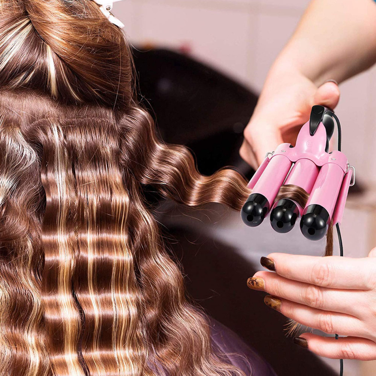 Ein Stylist verwendet einen rosa Haarkrepper am Haar einer Frau, um gewellte Krausen zu erzeugen. Das Haar ist braun.