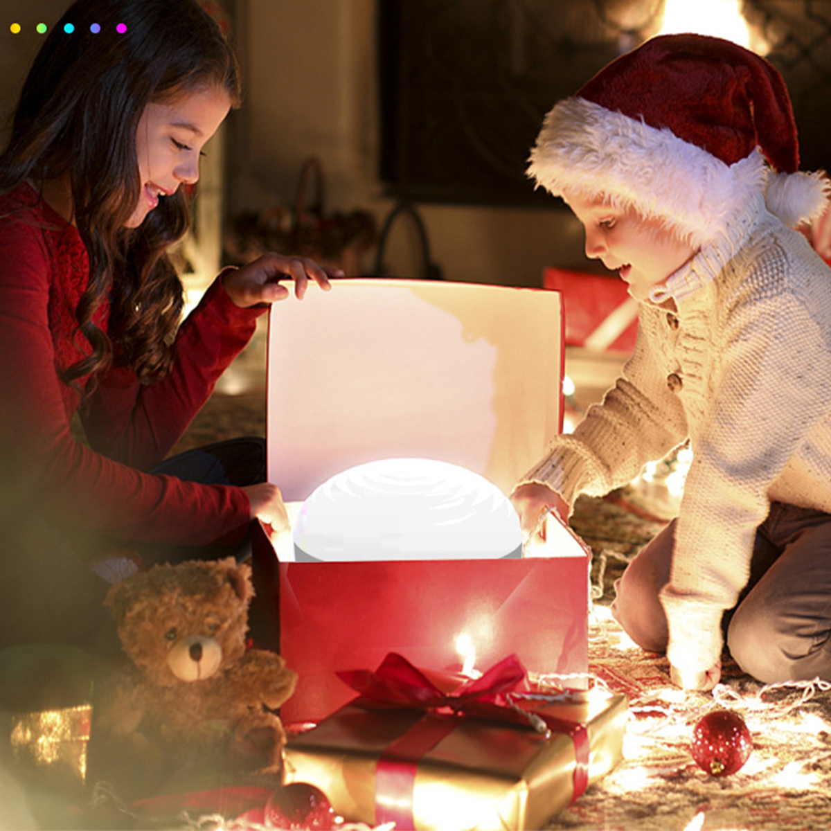 Zwei Kinder öffnen eine Geschenkbox mit einem leuchtenden Licht darin. Ein Teddybär ist vorhanden.