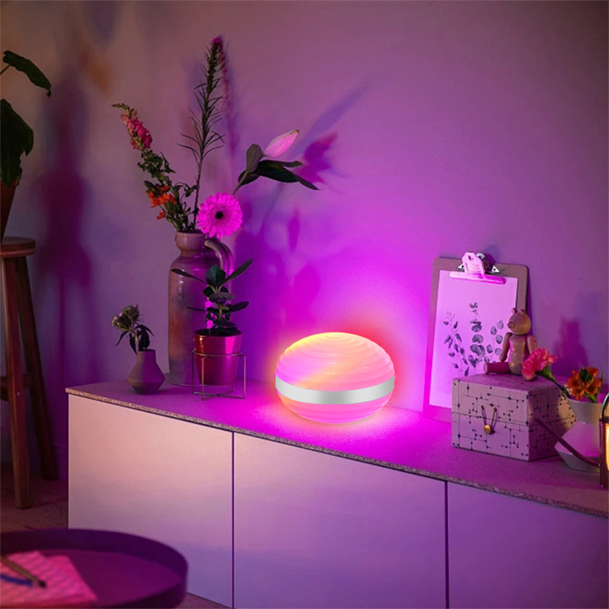 Eine runde, beleuchtete Lampe mit pink-lila Farbverlauf auf weißer Oberfläche.