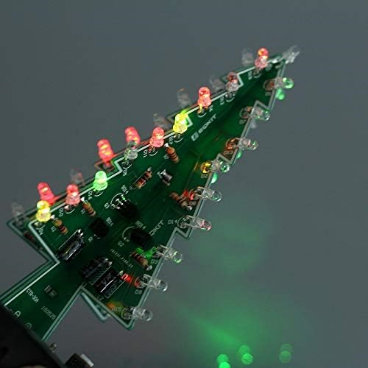 Eine grüne, weihnachtsbaumförmige Leiterplatte mit bunten Lichtern. Der Hintergrund ist grau.