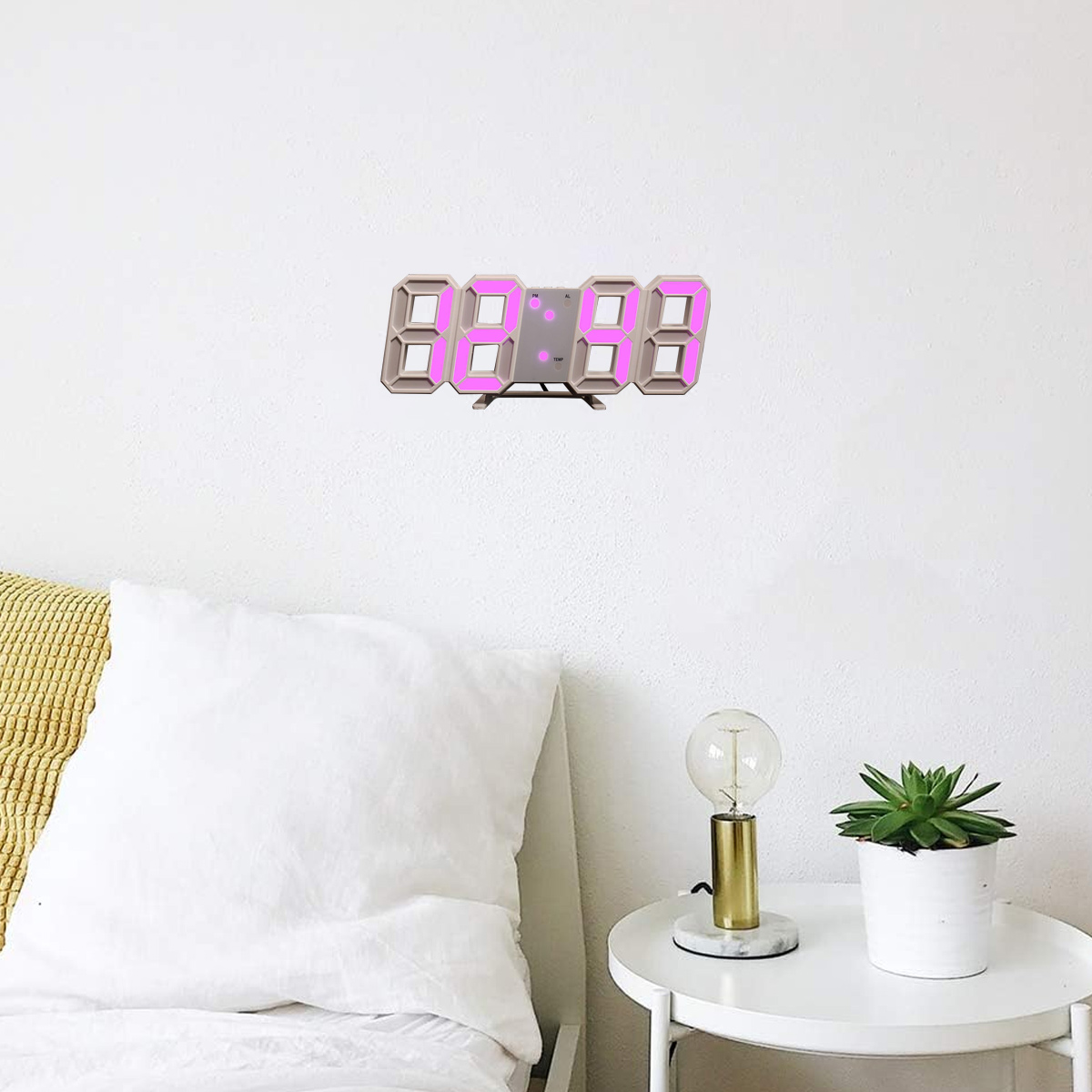 Digitaluhr an einer weißen Wand mit rosa Zahlen. Ein Tisch mit Lampe und Pflanze darunter.