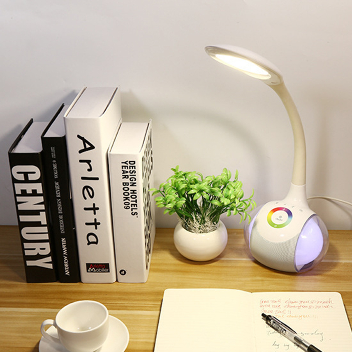 Eine weiße Schreibtischlampe neben Büchern und einer Pflanze, mit Notizbuch und Stift.