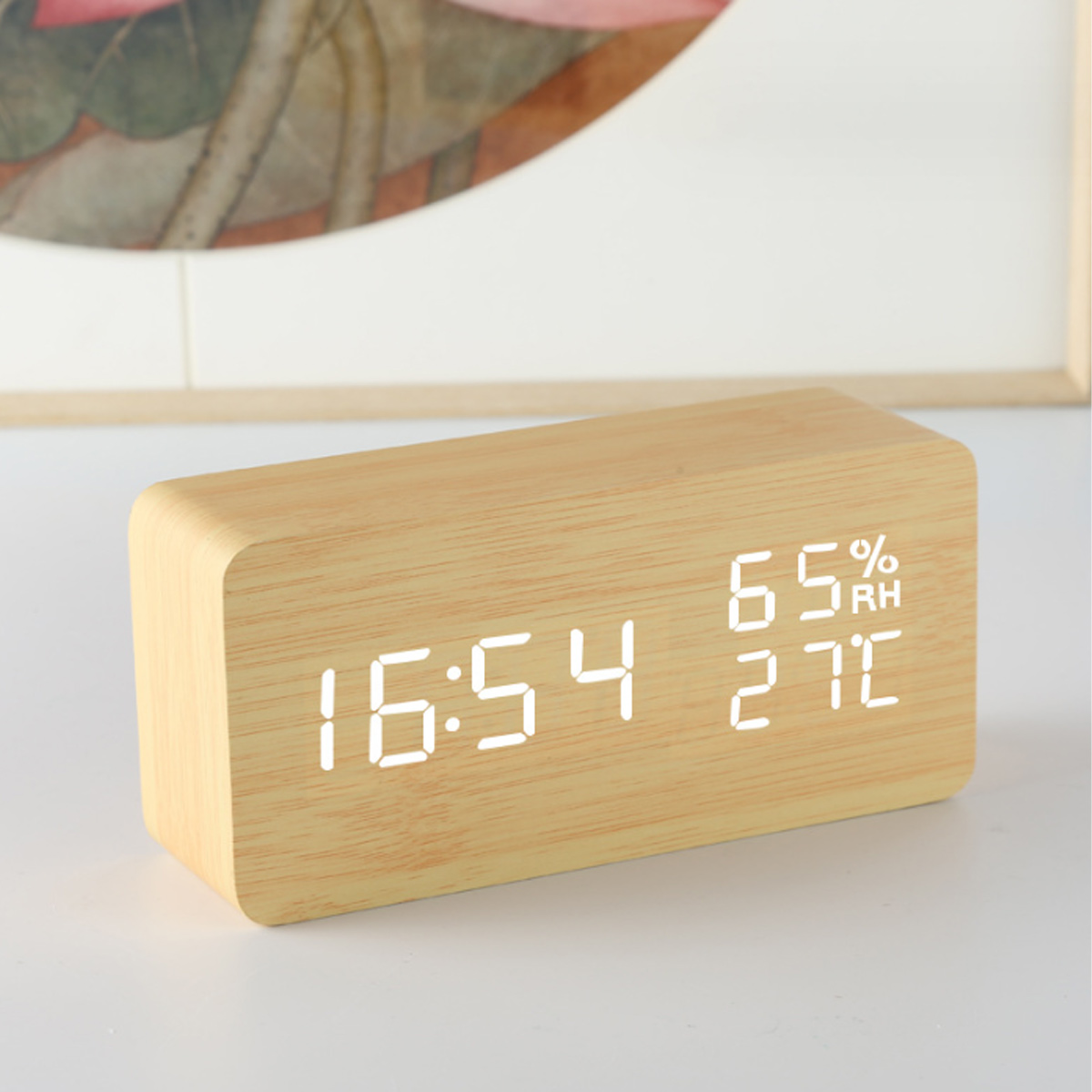 Digitaluhr aus Holz, zeigt 16:54, 65% RH und 27C an. Auf weißer Oberfläche, unscharfer Hintergrund.