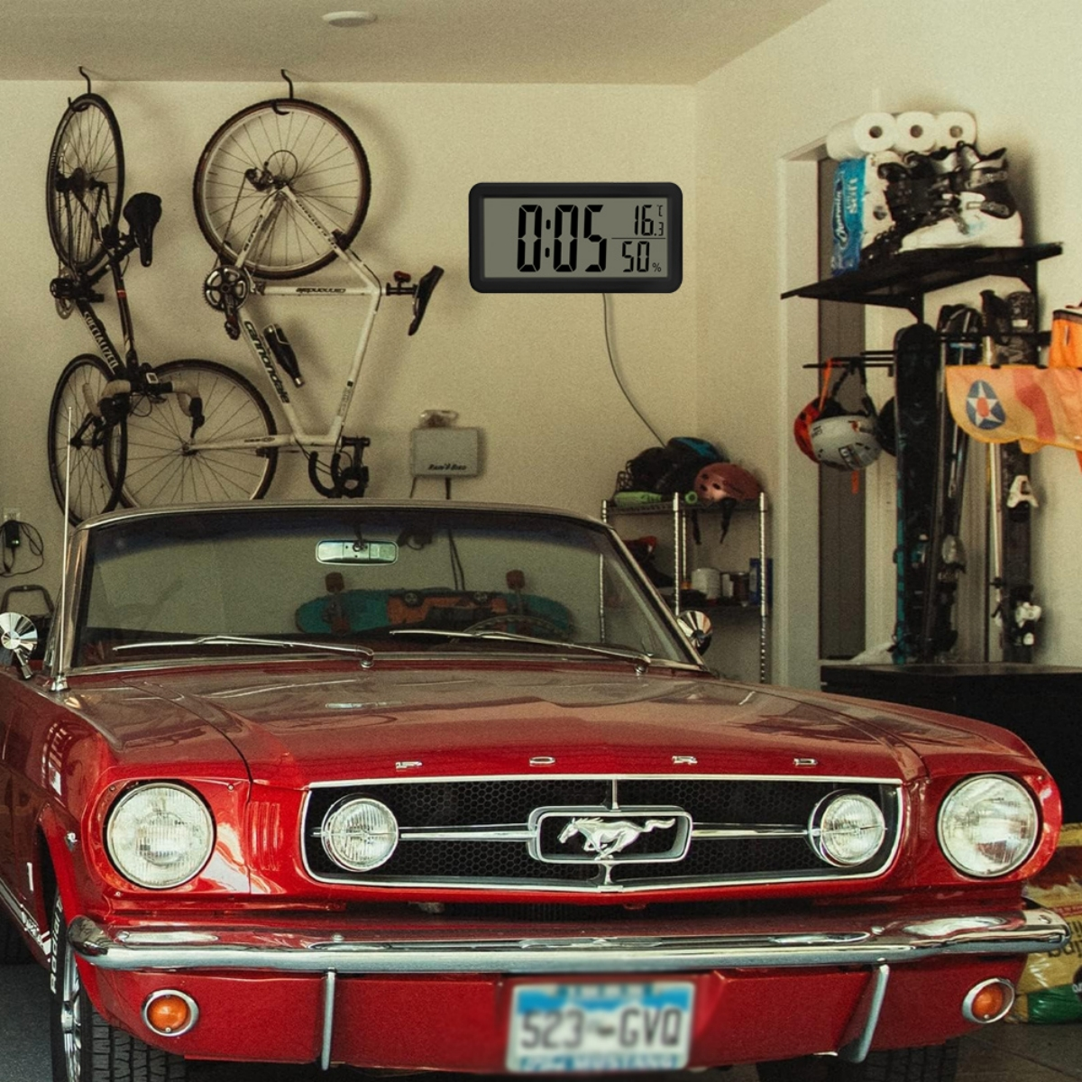 Roter Oldtimer in einer Garage mit Fahrrädern und einer Digitaluhr geparkt.