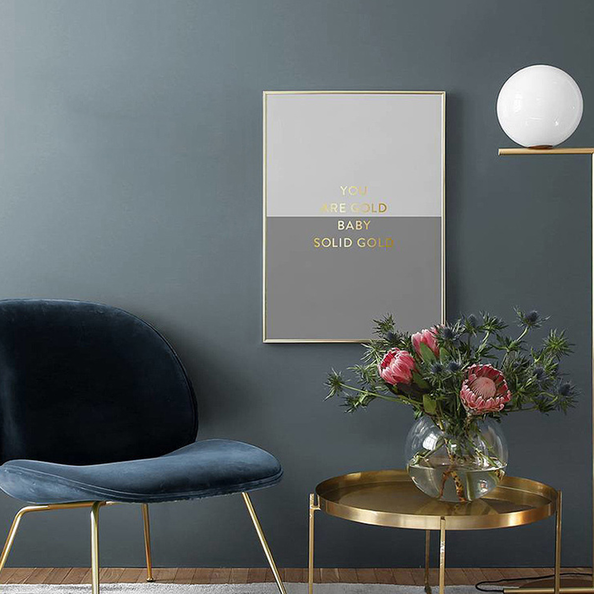 Ein gerahmtes Kunstwerk an einer Wand mit einer Blumenvase. Das Kunstwerk hat goldenen Text auf grauen und weißen Feldern.