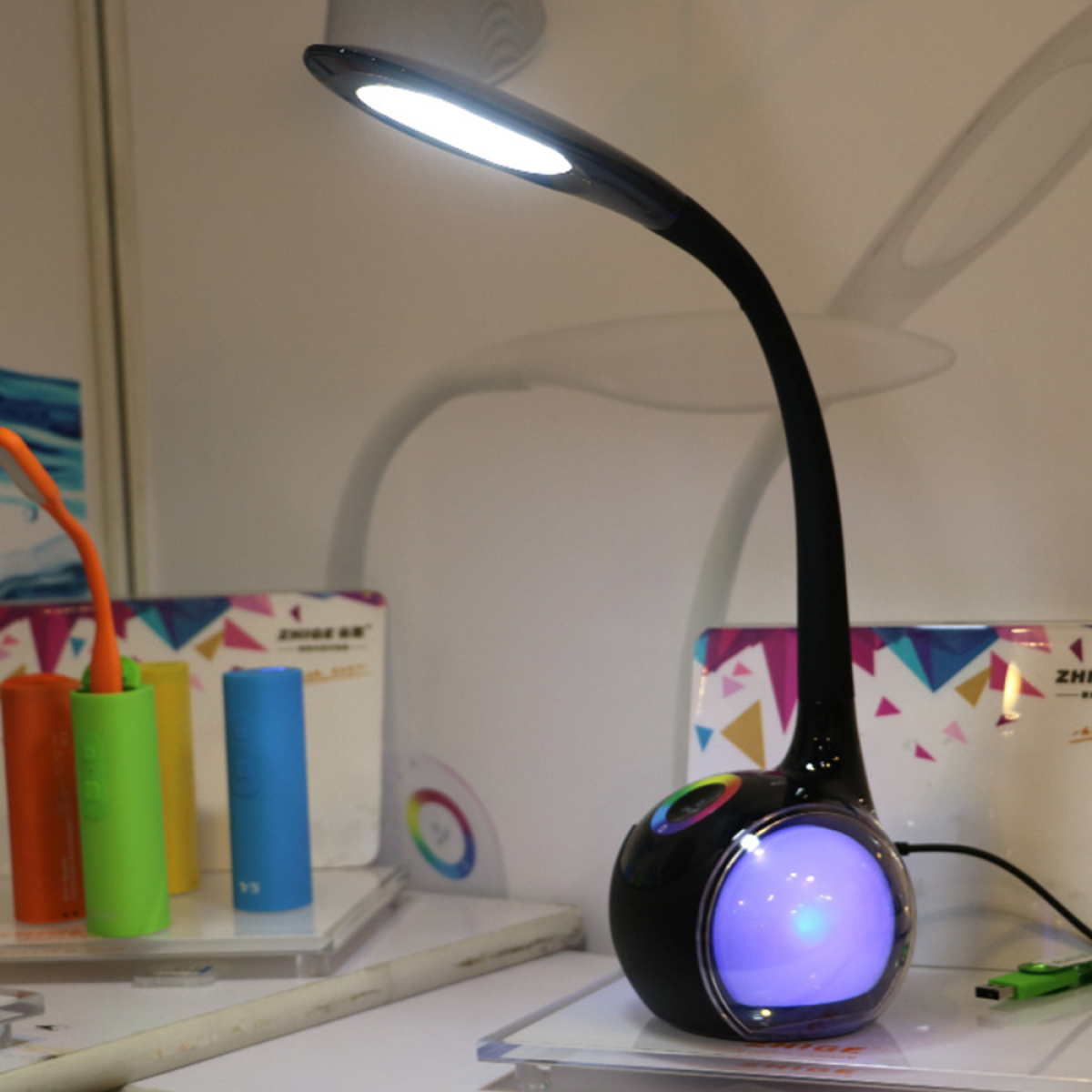 Schwarze Schreibtischlampe mit gebogenem Hals. Die Lampe hat ein weißes Licht und ein farbiges Licht in der Basis.