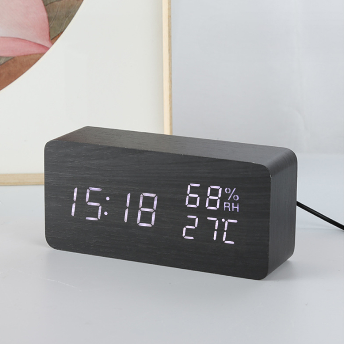 Schwarze Holzuhr, die Zeit, Datum und Temperatur anzeigt. Die Uhr befindet sich auf einer weißen Oberfläche.