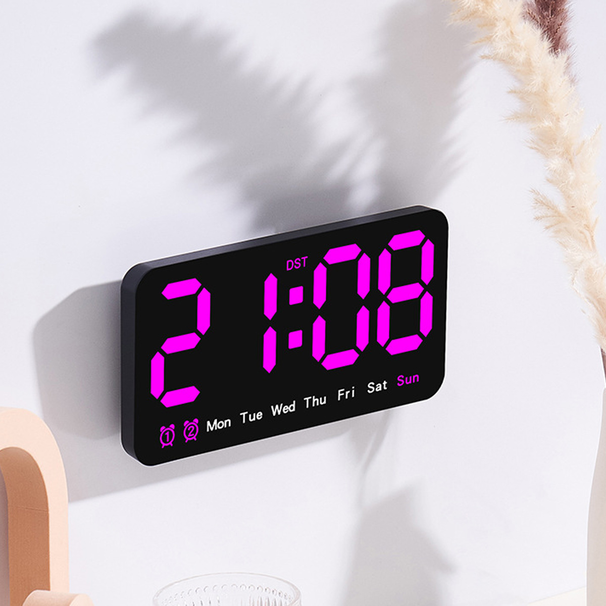 Schwarze Digitaluhr zeigt Zeit und Wochentag an, mit schwarzem Rahmen und weißer Wand.