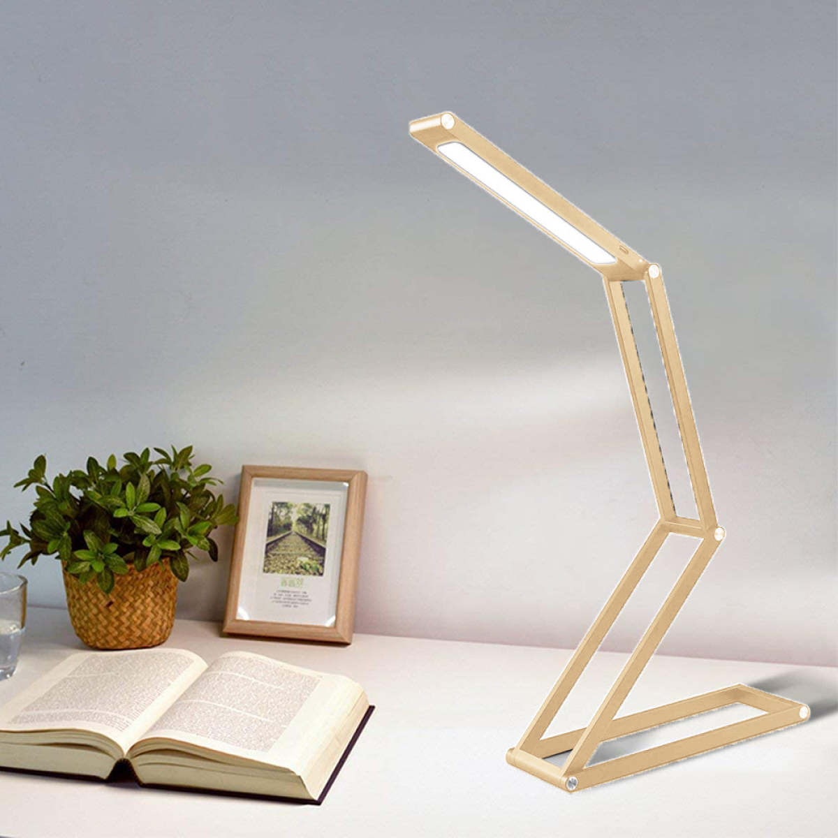 Eine goldene Schreibtischlampe auf einem weißen Schreibtisch mit einem Buch und Pflanzen.